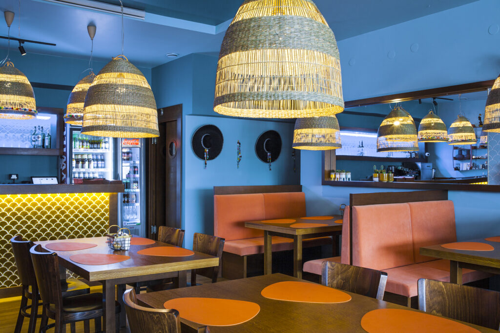 Sala restauracji z pomarańczowymi lożami, plecionymi lampami i barem z kaflami w łuski